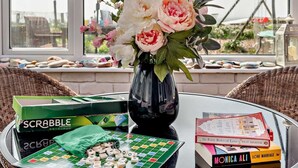 Scrabble-lautapeli, maljakko kukkineen ja kirjoja pöydällä.