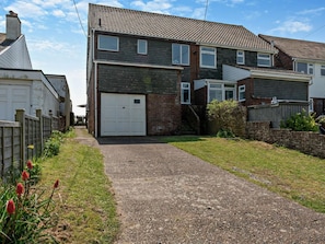 A two-story residential building with a garage, a gravel driveway, and a fenced yard. - 3 Bed in Pevensey (oc-93829) (Normans Bay)