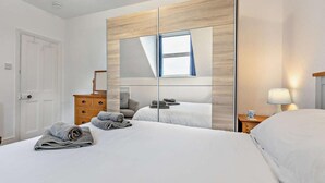 A hotel room with a large bed, a dresser, a mirror, and a nightstand with a lamp. - 2 Bed in Woolacombe (oc-76350) (Woolacombe)