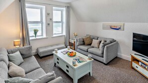 A modern living room with a grey sofa, a white coffee table, and a television on a wooden stand. - 2 Bed in Woolacombe (oc-76350) (Woolacombe)