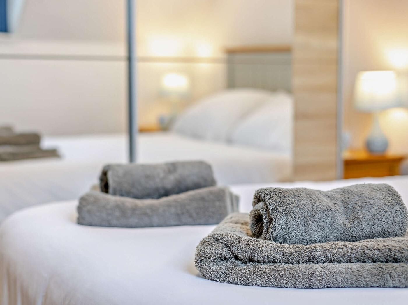 Une chambre d’hôtel avec un lit bien fait, un grand miroir qui reflète la pièce et une table de chevet avec une lampe.