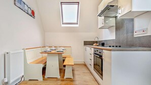 A compact kitchen with a dining table, a built-in oven, and a window above the sink. - 2 Bed in Woolacombe (oc-76350) (Woolacombe)