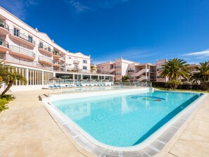 A swimming pool with lounge chairs, a building with balconies, and palm trees. - Apt. Luz da Manhã, with sea views (Luz)
