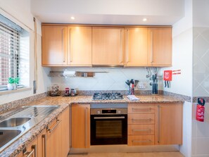 A modern kitchen with wooden cabinets, granite countertops, stainless steel appliances, and a window with blinds. - Apt. Luz da Manhã, with sea views (Luz)