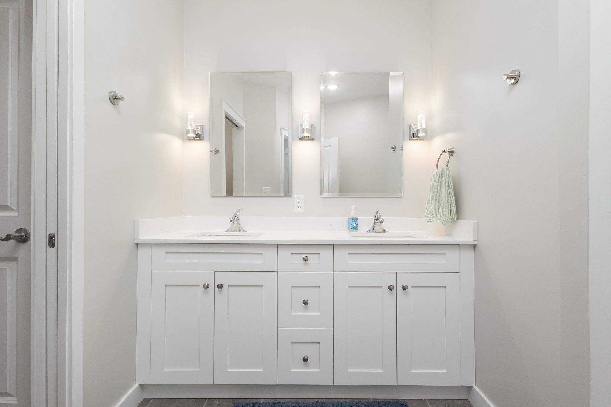 A bathroom with a white vanity, two mirrors, a towel rack, and a door.