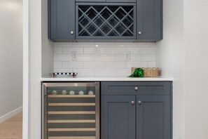 A kitchen with grey cabinets, a built-in wine cooler, white tiled backsplash, and a small basket on the countertop. - Golden View | 3BD • 2.5BA • Balcony (South Bend)