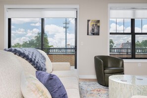 A living room with a sofa, a chair, a coffee table, and large windows with a view of a cityscape. - Golden View | 3BD • 2.5BA • Balcony (South Bend)