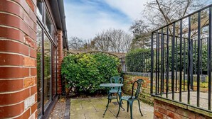 Un patio con un muro de ladrillo, una valla de metal y un arbusto verde.