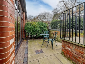 Eine Terrasse mit Backsteinmauer, Metallzaun und einem grünen Busch.