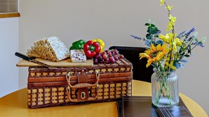 Una maleta de mimbre, pan, queso, pimientos, uvas y un florero con flores sobre una mesa.