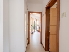 A hallway with a wooden door on the right, a white wall, and a view into a room with a curtain. - Casa Vista Linda | Private Sea View Villa & Saltwater Pool (LUZ-LGS)