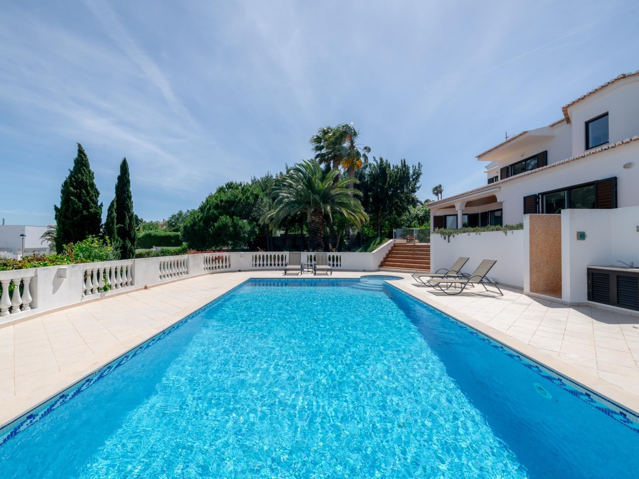 A rectangular swimming pool with a tiled deck, surrounded by a white wall with a balustrade.