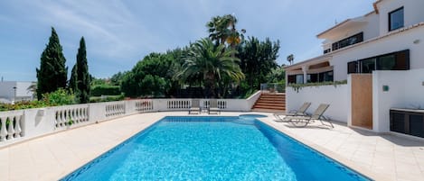 A rectangular swimming pool with a tiled deck, surrounded by a white wall with a balustrade.