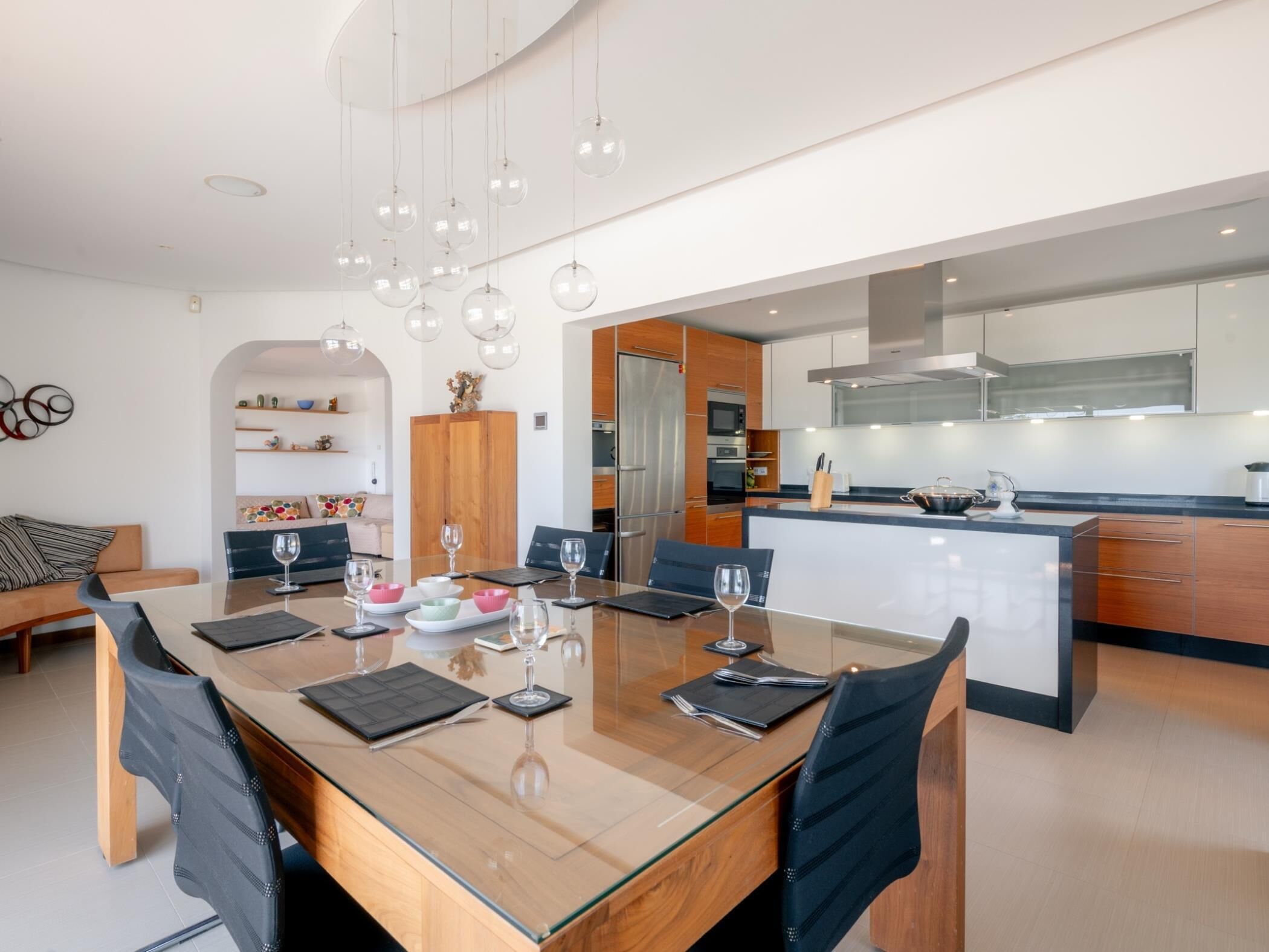 A modern kitchen with a central island, built-in appliances, and a dining area with a glass table and chairs.