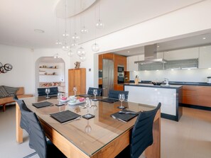 A modern kitchen with a central island, built-in appliances, and a dining area with a glass table and chairs. - Casa Vista Linda | Private Sea View Villa & Saltwater Pool (LUZ-LGS)