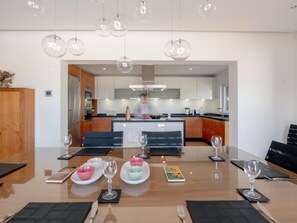 Un espace repas moderne avec une grande table, plusieurs chaises et une cuisine en arrière-plan.