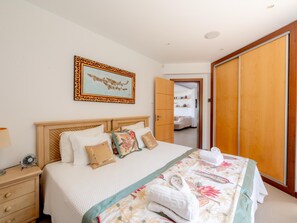 A hotel room with a bed, a bedside table, a lamp, a fan, a wardrobe, and a door leading to another room. - Casa Vista Linda | Private Sea View Villa & Saltwater Pool (LUZ-LGS)