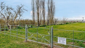 A fenced dog play area with a sign, metal gate, and trees in the background. - 2 Bed in Doncaster (oc-93770) (Mattersey)