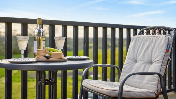 A balcony with a round table, two glasses, a bottle, and a chair. - 1 Bed in Sturminster Newton (oc-93841) (Hazelbury Bryan)