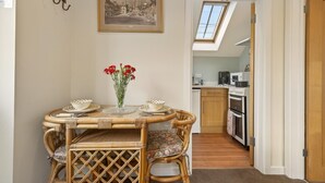 A dining area with a round table, wicker chairs, a vase with flowers, and a framed picture on the wall. - 1 Bed in Sturminster Newton (oc-93841) (Hazelbury Bryan)