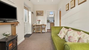 A living room with a television, a sofa, a dining table with chairs, a kitchen in the background, and a hallway leading to another room. - 1 Bed in Sturminster Newton (oc-93841) (Hazelbury Bryan)