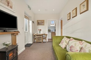 A living room with a television, a sofa, a dining table with chairs, a kitchen in the background, and a hallway leading to another room. - 1 Bed in Sturminster Newton (oc-93841) (Hazelbury Bryan)