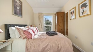 A bedroom with a bed, a nightstand, a window with curtains, and framed artwork on the walls. - 1 Bed in Sturminster Newton (oc-93841) (Hazelbury Bryan)