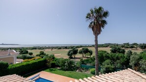 A pool with a view of the sea, a palm tree, and a golf course. - Villa Sea La Vie | Exclusive Villa with Private Pool near Palmares Golf Course (Vale da Lama - Odiáxere)