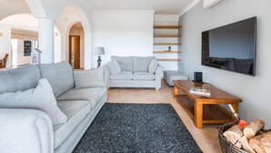 A modern living room with a grey sofa, a smaller grey sofa, a wooden coffee table, and a TV mounted on the wall. - Villa Sea La Vie | Exclusive Villa with Private Pool near Palmares Golf Course (Vale da Lama - Odiáxere)