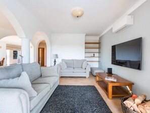 A modern living room with a grey sofa, a smaller grey sofa, a wooden coffee table, and a TV mounted on the wall. - Villa Sea La Vie | Exclusive Villa with Private Pool near Palmares Golf Course (Vale da Lama - Odiáxere)