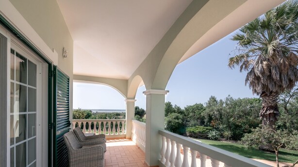 A covered balcony with a view of the sea, a wicker sofa, and a palm tree. - Villa Sea La Vie | Exclusive Villa with Private Pool near Palmares Golf Course (Vale da Lama - Odiáxere)