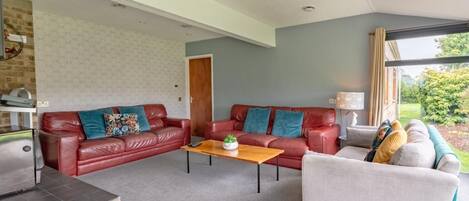 Un salón con un sofá de cuero rojo, un sillón blanco y una mesa de centro de madera.