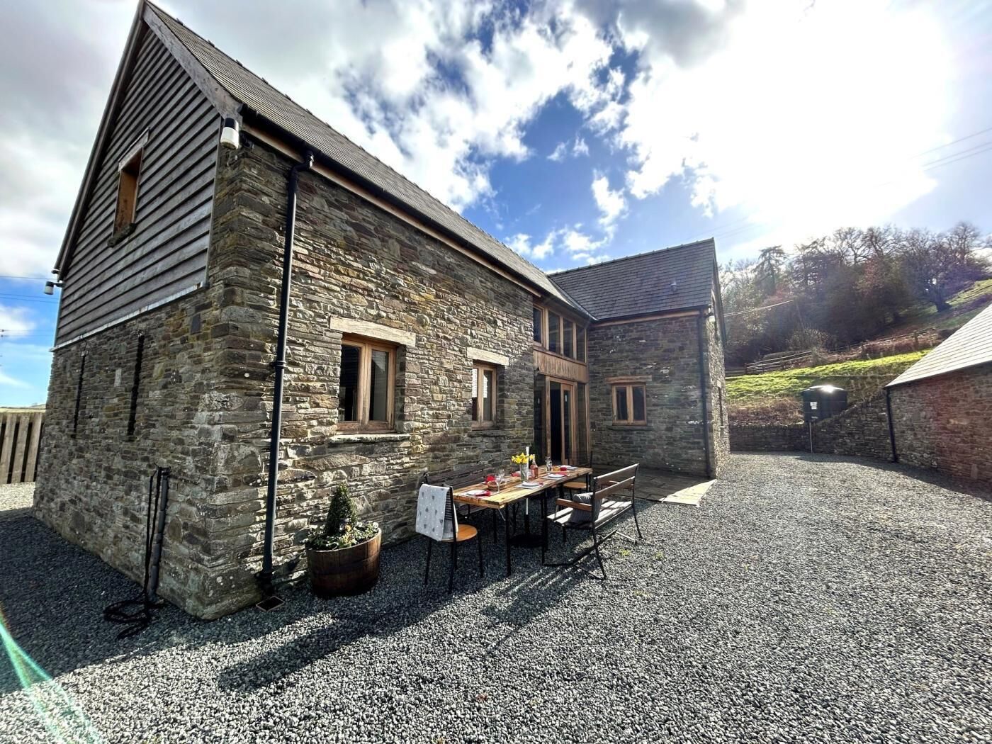 A stone building with a gravel courtyard, a table with chairs, and a potted plant.