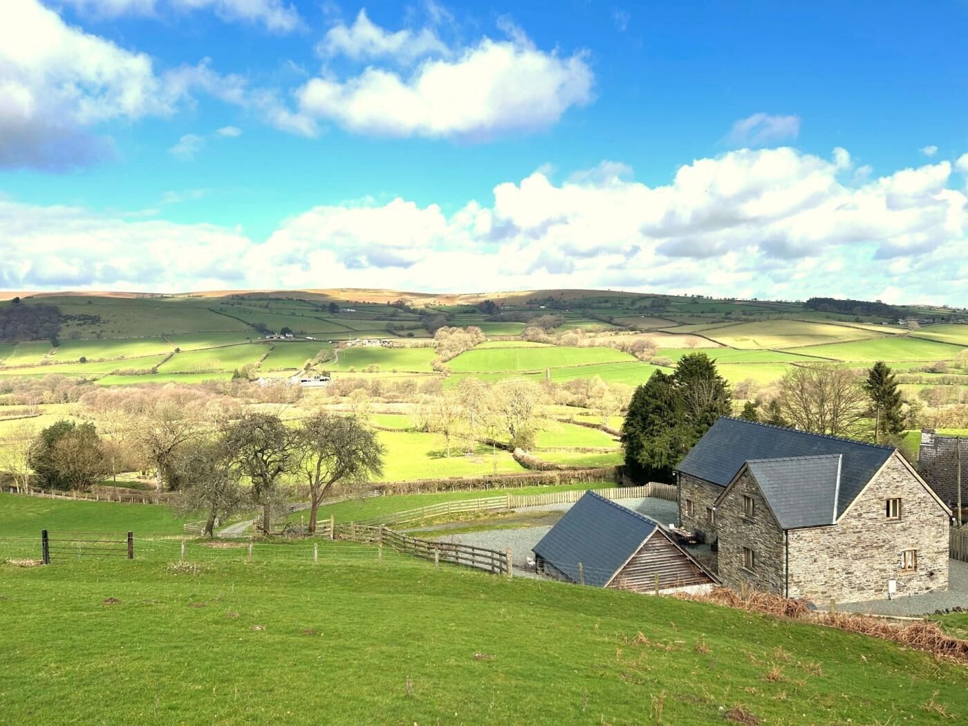 Un paysage rural avec une maison en pierre, des champs verdoyants et un ciel dégagé.