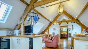 Spazioso loft con cucina, zona pranzo e soggiorno, caratterizzato da travi in legno, un lampadario e un'ampia finestra.