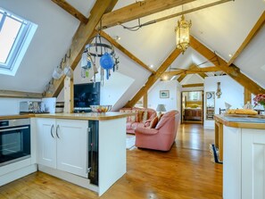 A spacious loft with a kitchen, dining area, and living room, featuring wooden beams, a chandelier, and a large window. - 4 Bed in Stroud (oc-93690) (Burcombe)