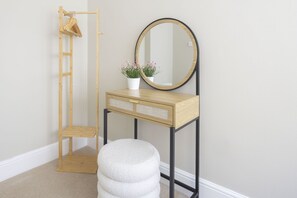 A room with a wooden vanity, a round mirror, a small stool, a wooden hanger rack, and a potted plant. - Stylish Two Bed Apartment on Montpellier Spa Road (Cheltenham)