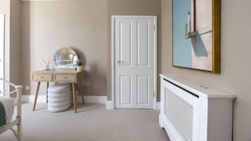 A room with a white door, a desk with a mirror, a radiator, and a painting on the wall.