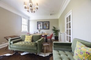 A living room with a green sofa, a wooden coffee table, and a dining area with a wooden table and chairs. - Stylish Two Bed Apartment on Montpellier Spa Road (Cheltenham)