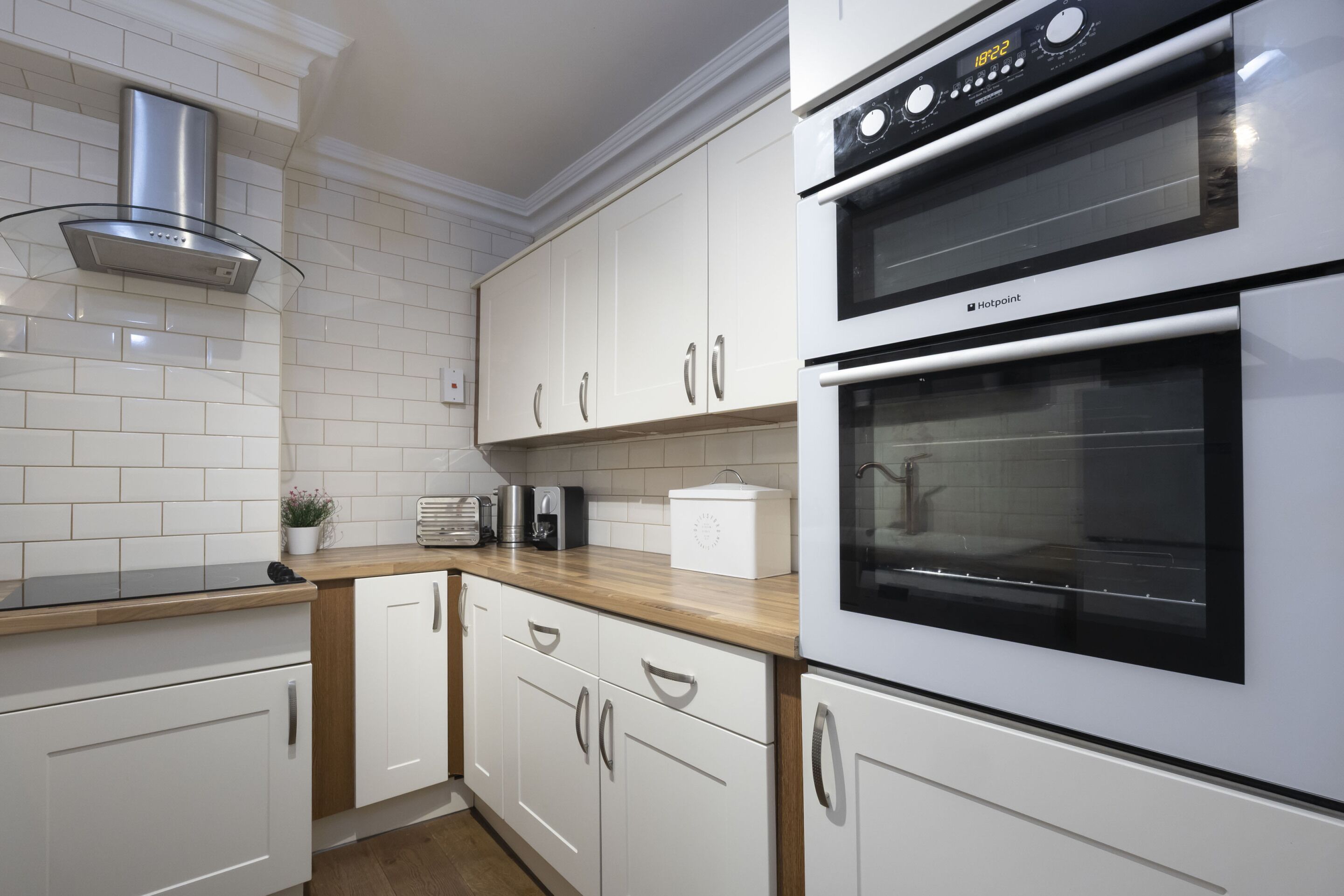 Een moderne keuken met witte kasten, een roestvrijstalen afzuigkap, een dubbele oven en een houten aanrecht.