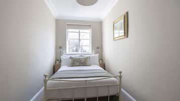 Een slaapkamer met een enkel bed, een raam, een nachtkastje en een lijst met een afbeelding aan de muur.