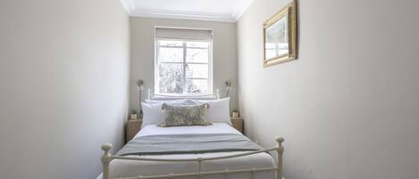 Een slaapkamer met een enkel bed, een raam, een nachtkastje en een lijst met een afbeelding aan de muur.