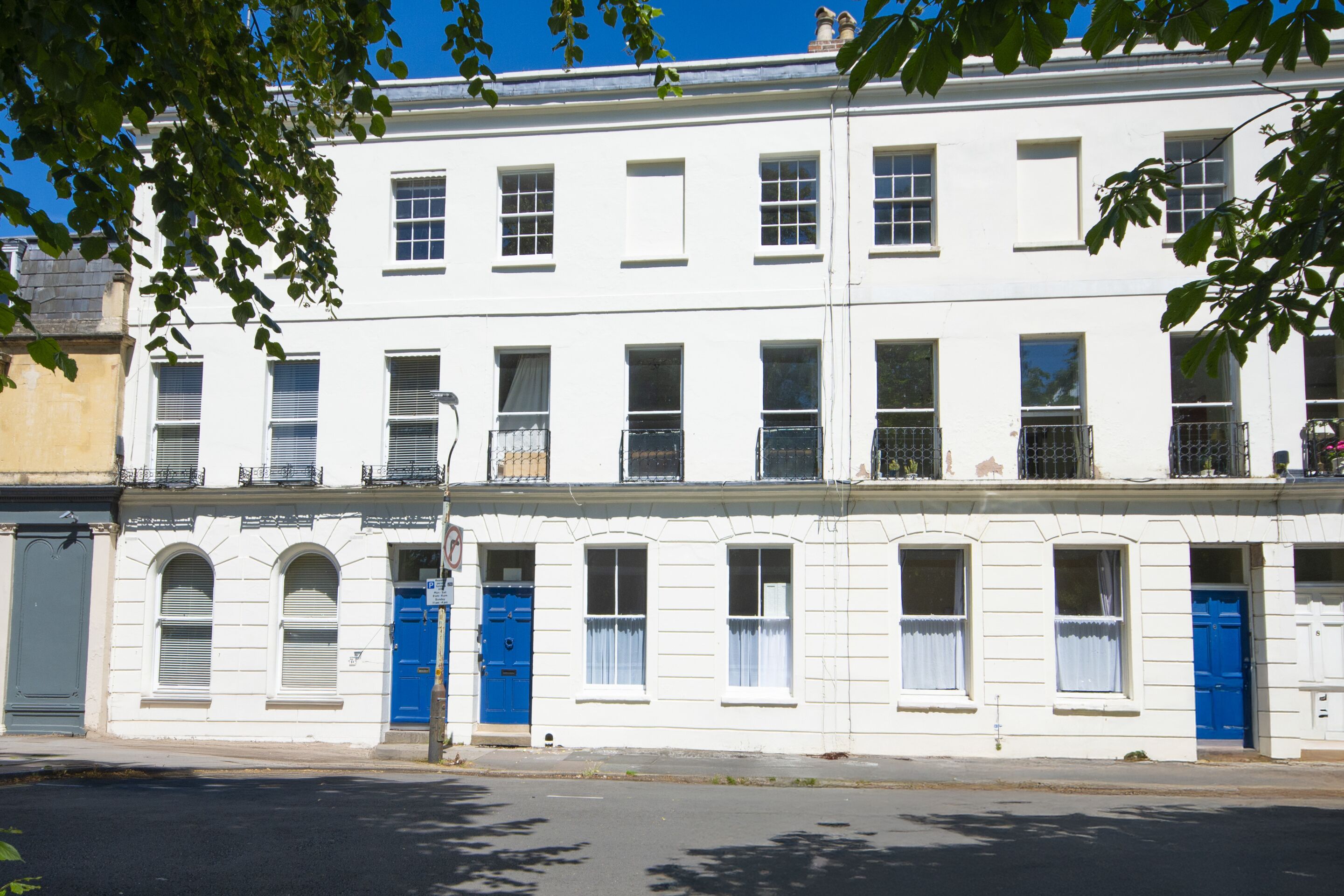 A row of white buildings with blue doors and windows, a clear sky, and a street in front.
