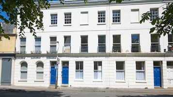 A row of white buildings with blue doors and windows, a clear sky, and a street in front.