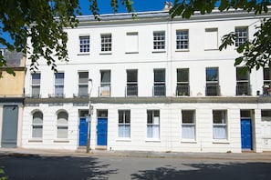 A row of white buildings with blue doors and windows, a clear sky, and a street in front. - Stylish Two Bed Apartment on Montpellier Spa Road (Cheltenham)