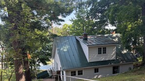 Een huis met een schuin dak, een pad dat ernaar leidt, en uitzicht op de omliggende bomen en lucht.