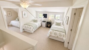 Een slaapkamer met twee bedden, een plafondventilator, een raam en een nachtkastje.