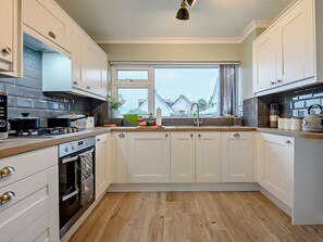A modern kitchen with white cabinetry, a gas stove, a built-in oven, and a window with a view of houses. - 3 Bed in Swanage (oc-93866) (Swanage)
