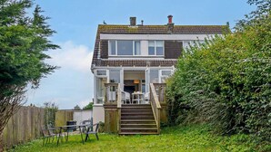 Ein zweistöckiges Haus mit Veranda, Treppe und umzäunter Garten.