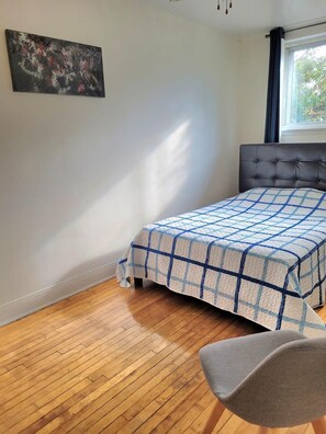 A bedroom with a bed, a chair, a window, and a painting on the wall.